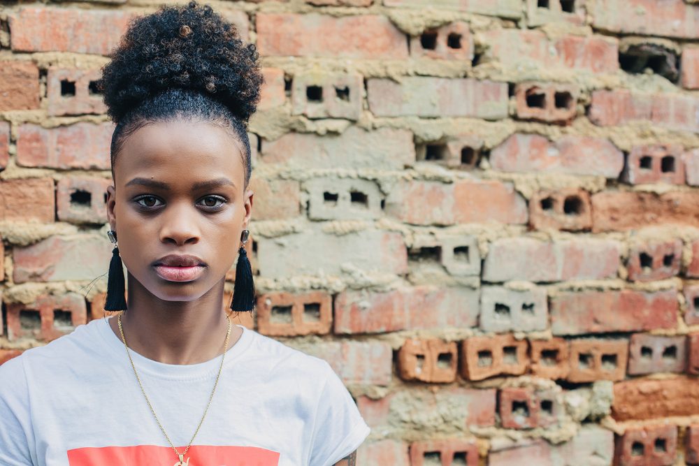 portrait of cheerful black teenage female with healthy-looking skin and voluminous African hair on brick wall background